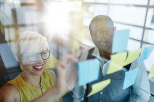 Two creative millennial small business owners working on social media strategy brainstorming using adhesive notes in windows